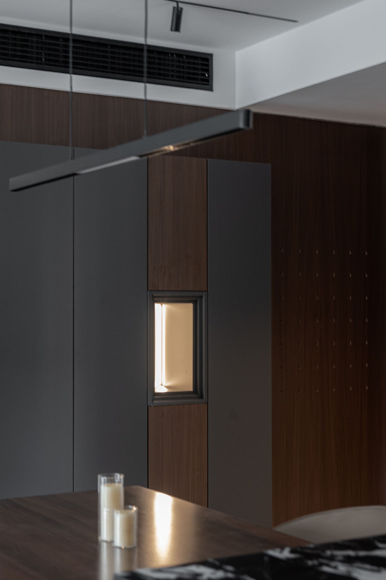 Lit niche in smoked oak and charcoal joinery above a dark dining table with candles