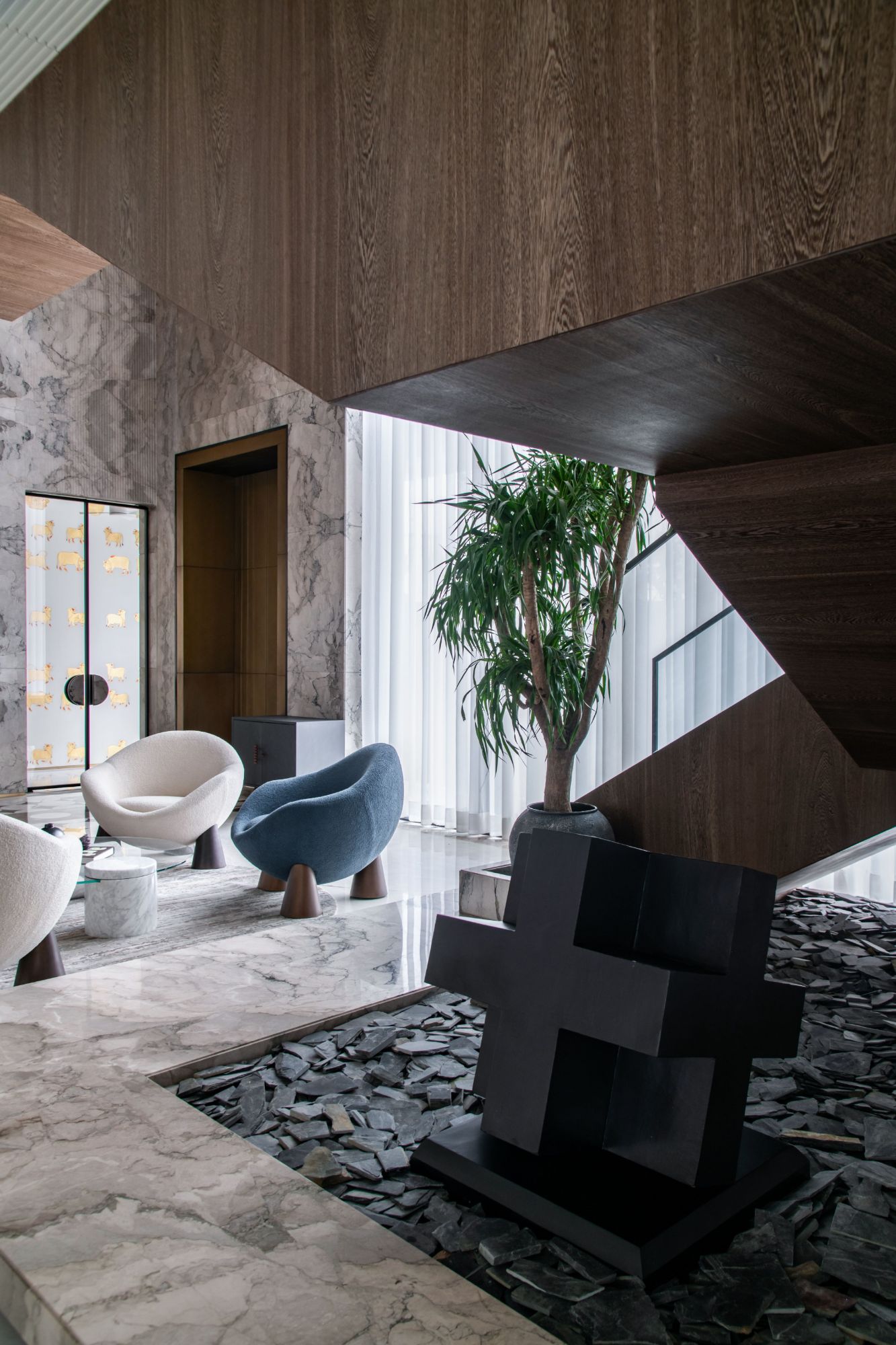 Double-height living room with a smoked oak stair, bouclé lounge chairs, marble floors and a black sculpture set in slate