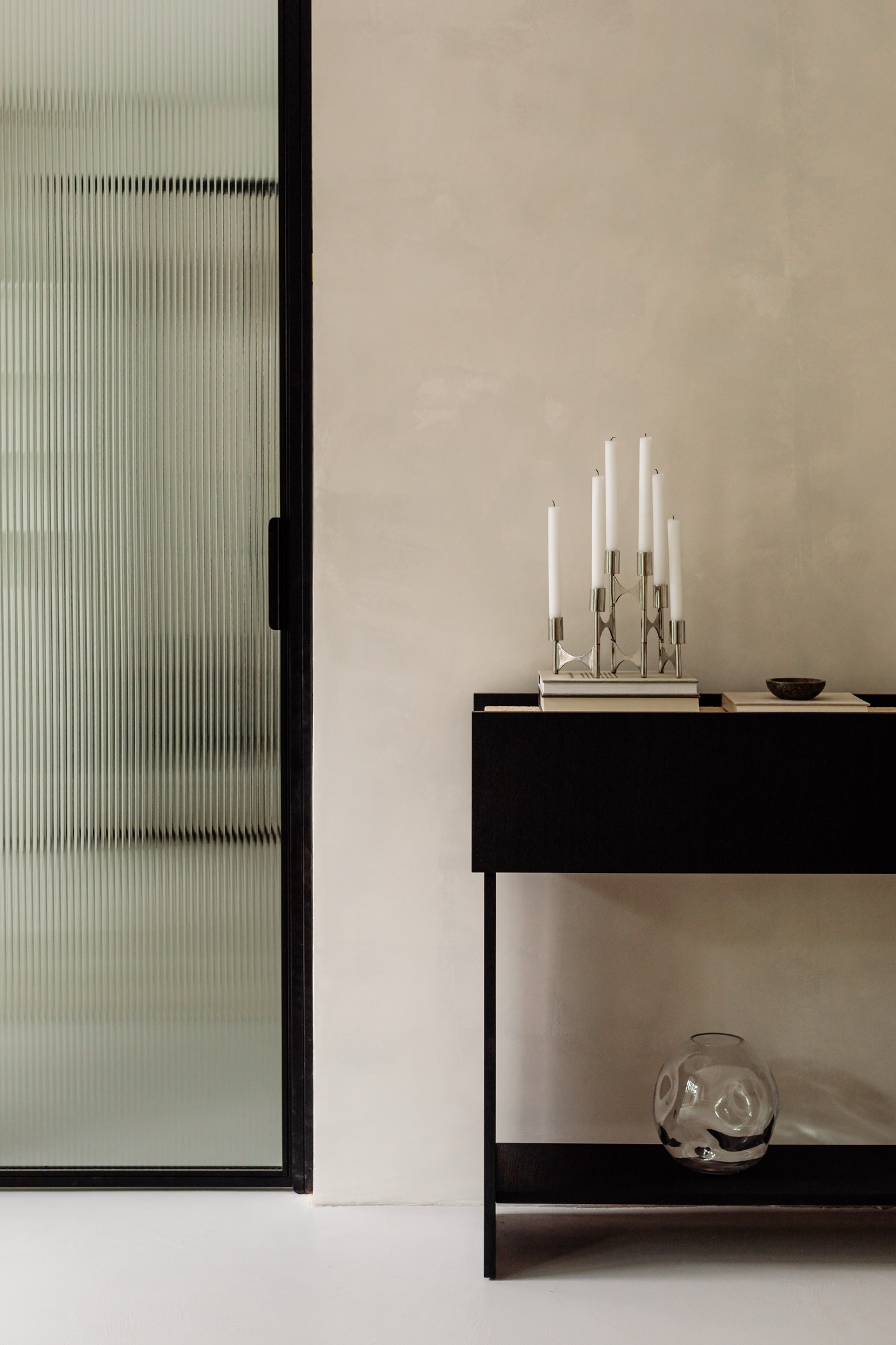 Ebonised oak console with candelabra beside a steel-framed reeded glass door against plaster