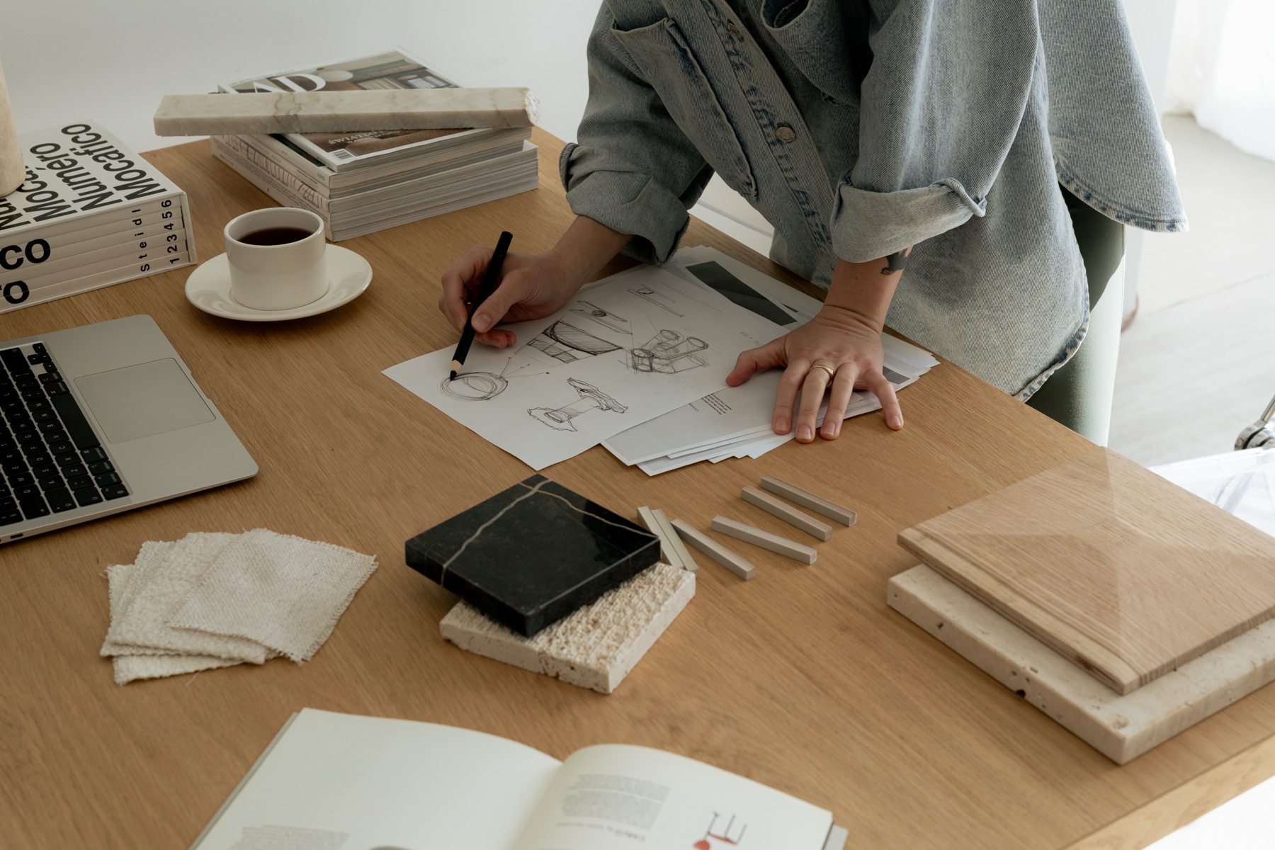 Sketching furniture details at the oak studio table among travertine, marble, oak and linen samples