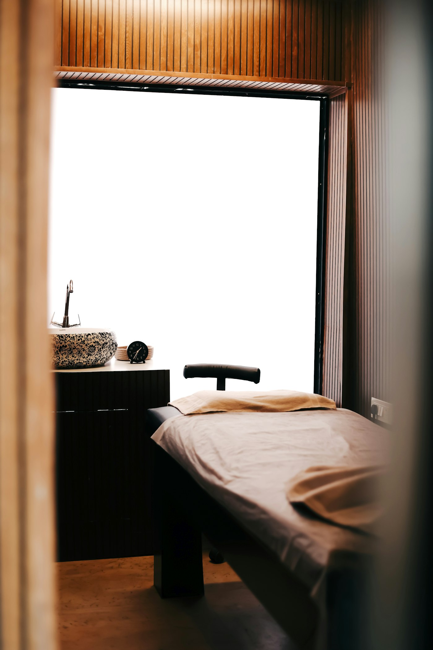 Quiet treatment room with a made-up facial bed beside a stone sink