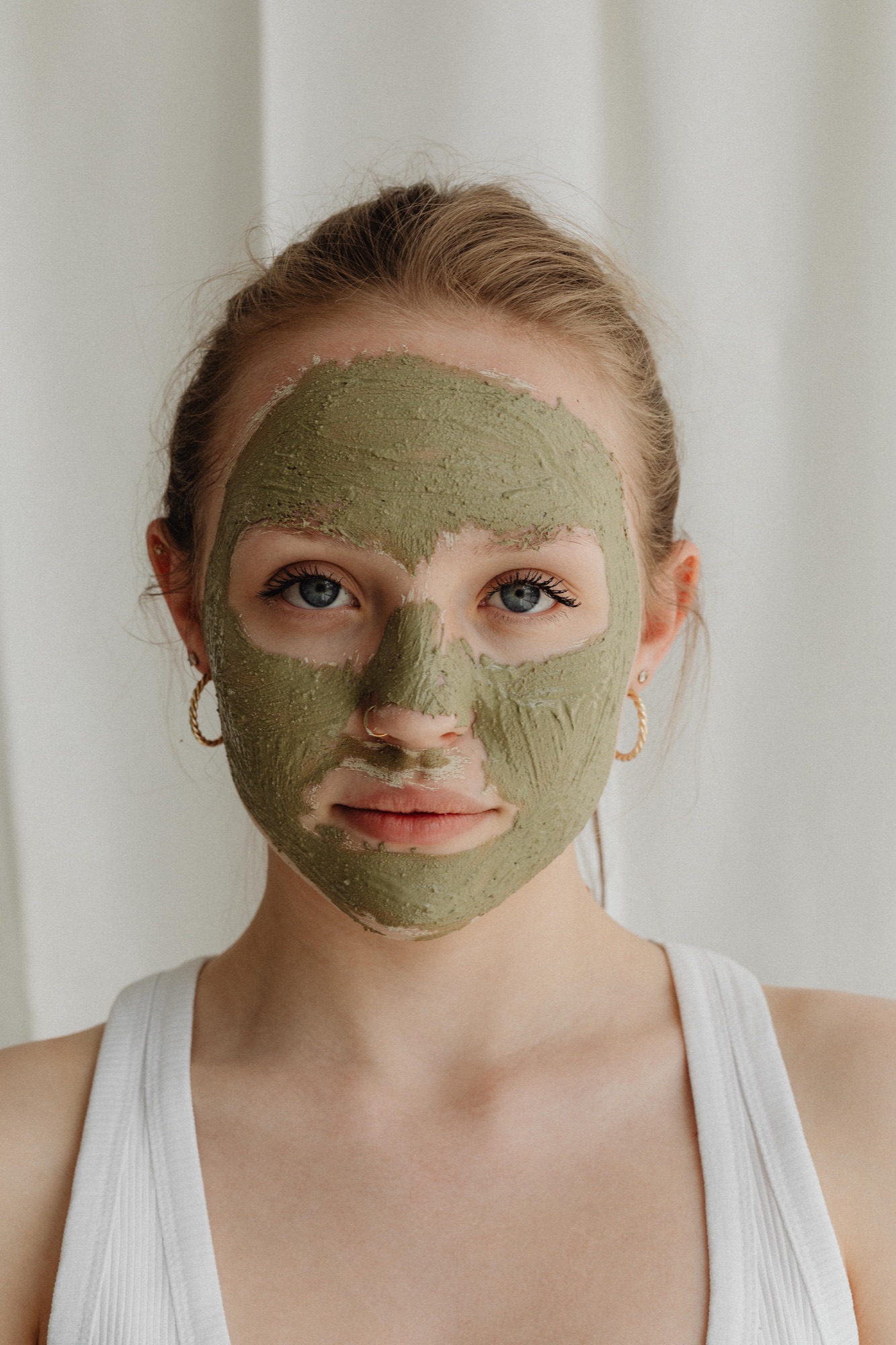 Woman wearing a green clay mask, looking into the camera