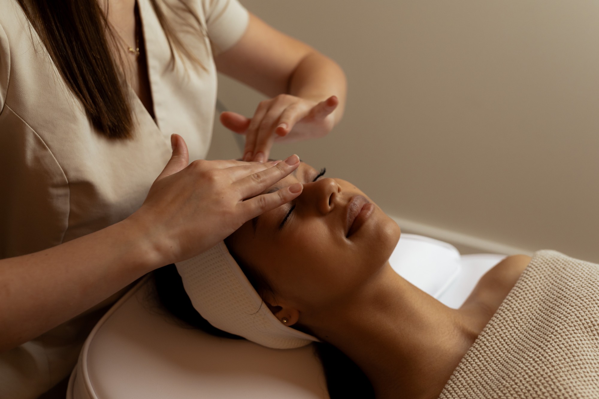 Esthetician’s hands resting on a client’s brow during a facial massage